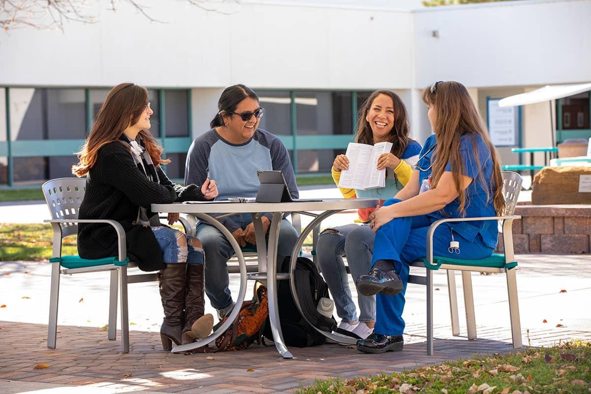 Four 火博体育 students sitting at a table outside conversing and smiling.